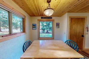 A dining area with a wooden table and chairs, a window with a view of trees, and a wooden ceiling. - Frazier Lake | Wallowa Lake rental (Joseph)
