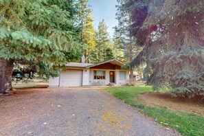 A small cabin with a gravel driveway, surrounded by tall evergreen trees. - Frazier Lake | Wallowa Lake rental (Joseph)