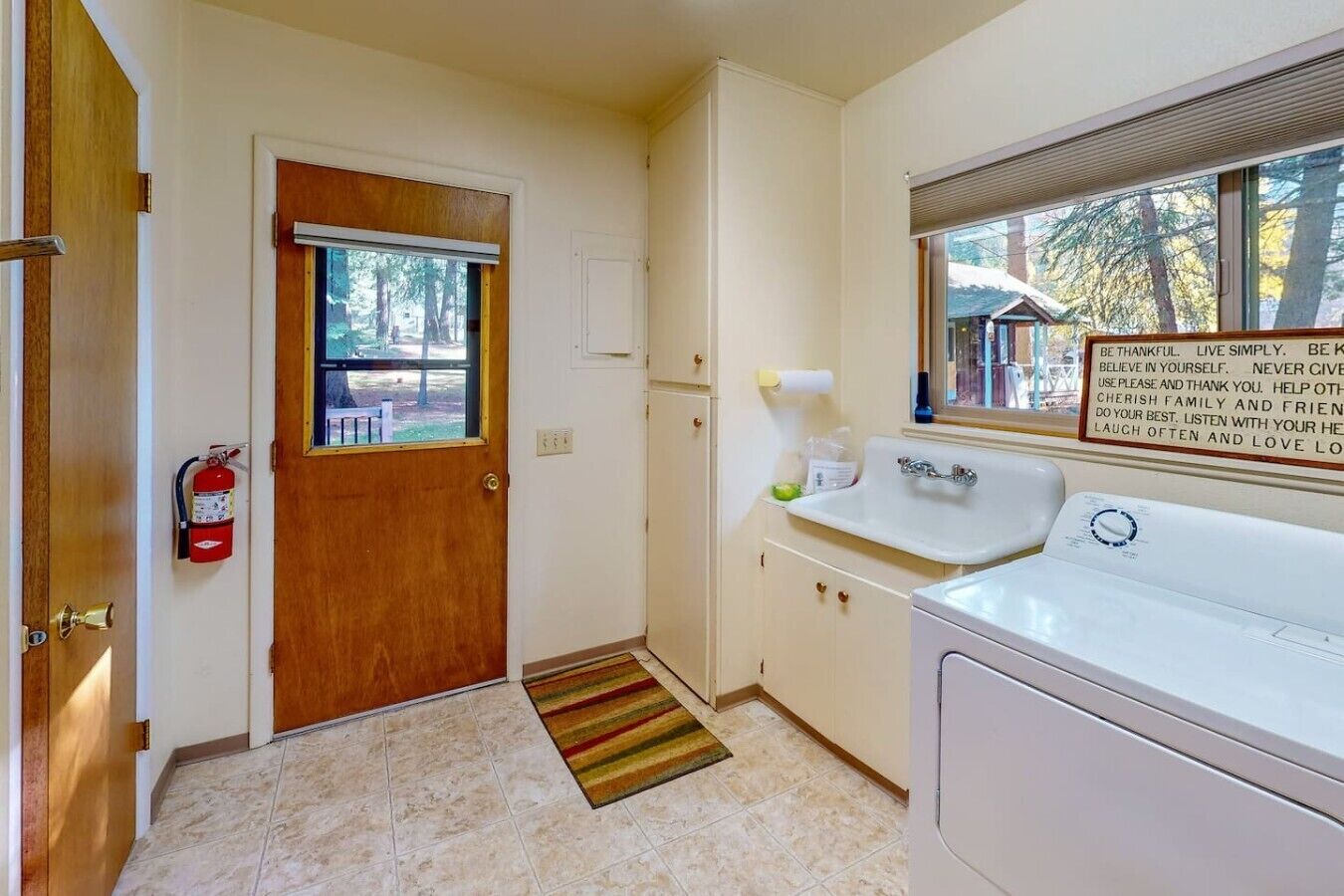 A small, clean room with a wooden door, a white sink, a window, and a fire extinguisher.