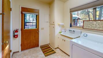 A small, clean room with a wooden door, a white sink, a window, and a fire extinguisher.