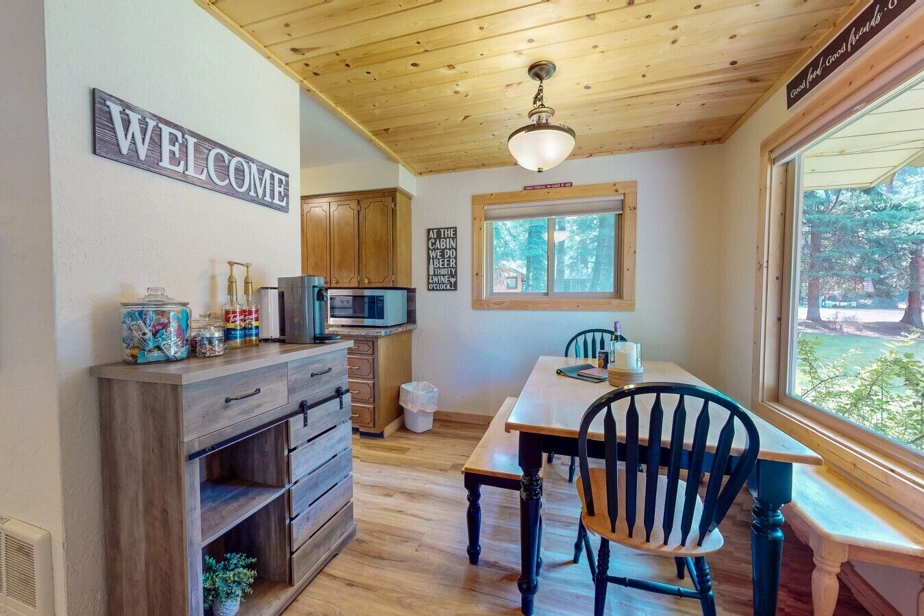 L’intérieur de la cabane est doté d’un plafond en bois, d’une pancarte de bienvenue, d’un coin cuisine avec un four à micro-ondes et d’une table à manger avec des chaises.