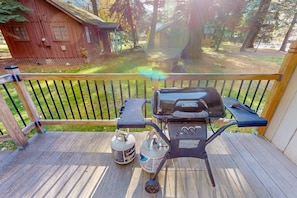 A wooden deck with a grill, propane tanks, and a small wooden cabin in the background. - Frazier Lake | Wallowa Lake rental (Joseph)