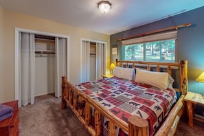A bedroom with a wooden bed frame, a quilt, a window with a view, and a closet. - Frazier Lake | Wallowa Lake rental (Joseph)