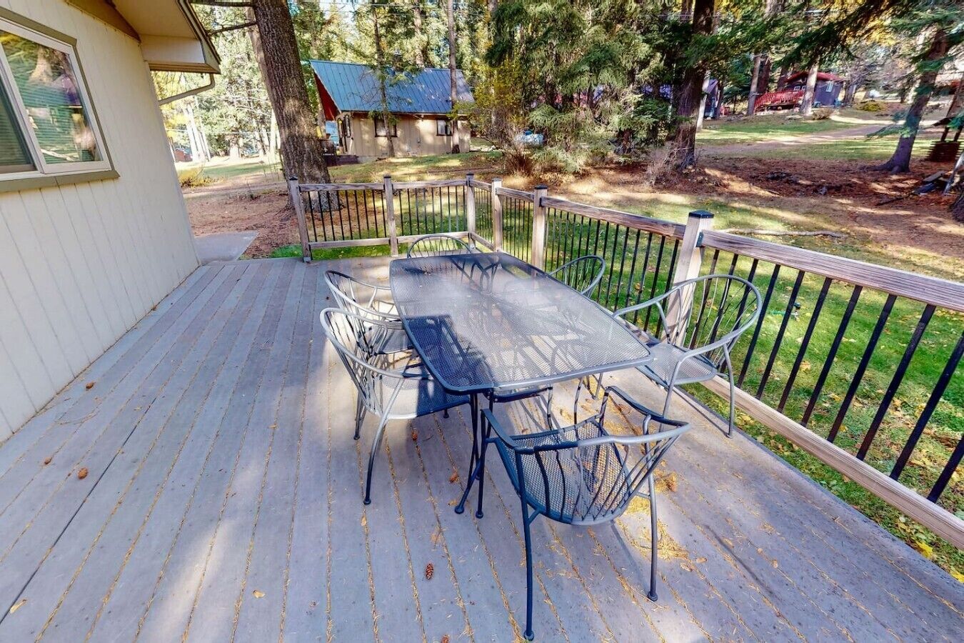 Une terrasse couverte avec une table et des chaises, entourée d’une plateforme en bois et d’une rambarde en métal.