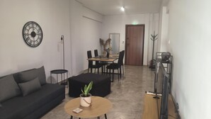A modern living room with a sofa, a coffee table with a plant, a dining area with chairs, and a TV on a wooden stand. - Casa Dili Stylish 2BR Apartment (Athens)