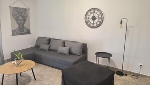 A modern living room with a grey sofa, a round coffee table, a small side table, a black ottoman, a wall clock, and a floor lamp. - Casa Dili Stylish 2BR Apartment (Athens)
