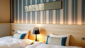 A hotel room with two beds, a nightstand with a lamp, and a wall with striped wallpaper and a framed picture. - oyado shinmachi gojo (Kyoto)
