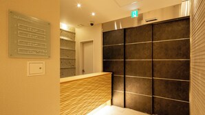 A reception area with a wooden reception desk, a wall-mounted information board, and a large dark-colored partition. - oyado shinmachi gojo (Kyoto)