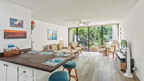 A modern living room with a dining area, large windows, and a ceiling fan. - *Kalanikai 215 | Kona Condo Near Downtown, Beaches and Dining (Kailua Kona)