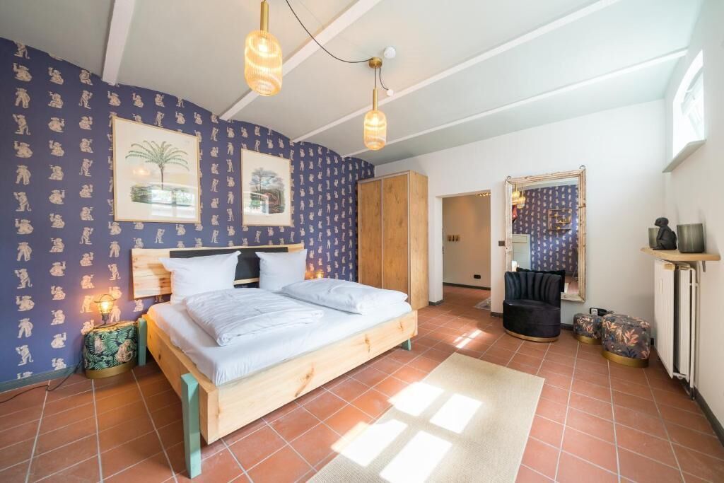 Een slaapkamer met een houten bed, nachtkastje, lamp, garderobe en een spiegel aan de muur.