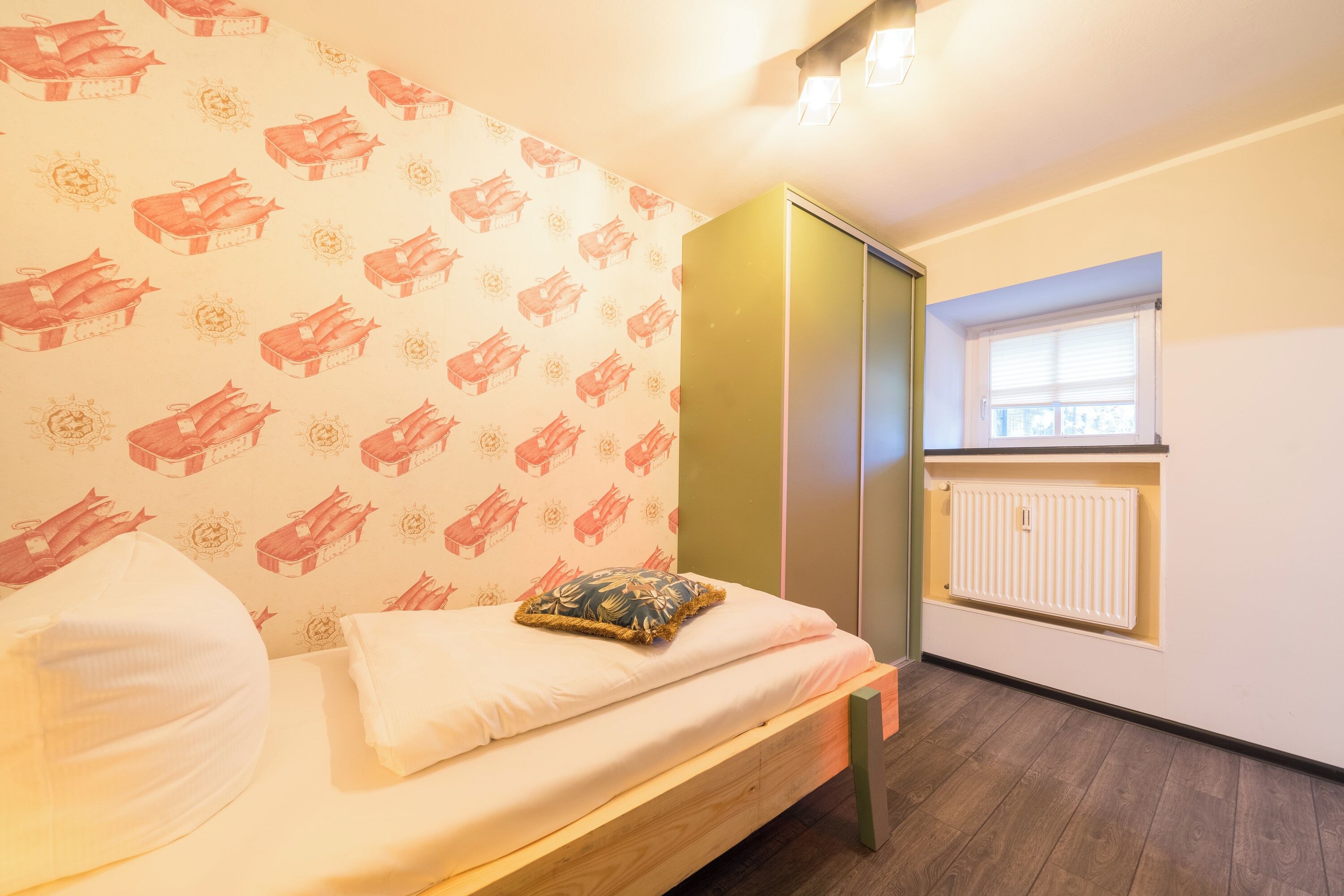 Un dormitorio con una cama, almohada, radiador y ventana.