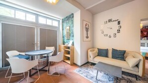 A modern living room with a sofa, a coffee table, and a dining area with chairs and a table. - Design Apartments - Remise Blumberg (Potsdam)