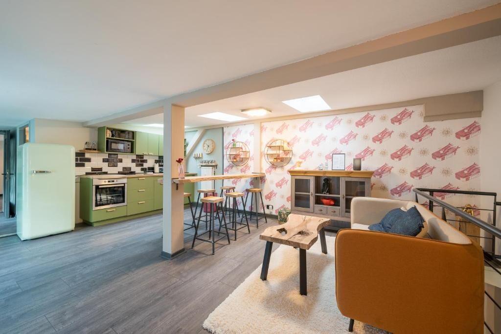 A modern kitchen with green cabinets, a white refrigerator, and a dining area with stools.