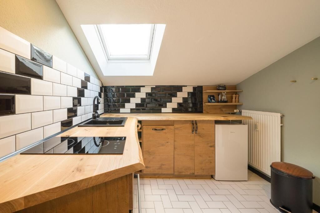 Una cocina compacta con tragaluz, salpicadero de baldosas blanco y negro, armarios de madera y lavavajillas integrado.