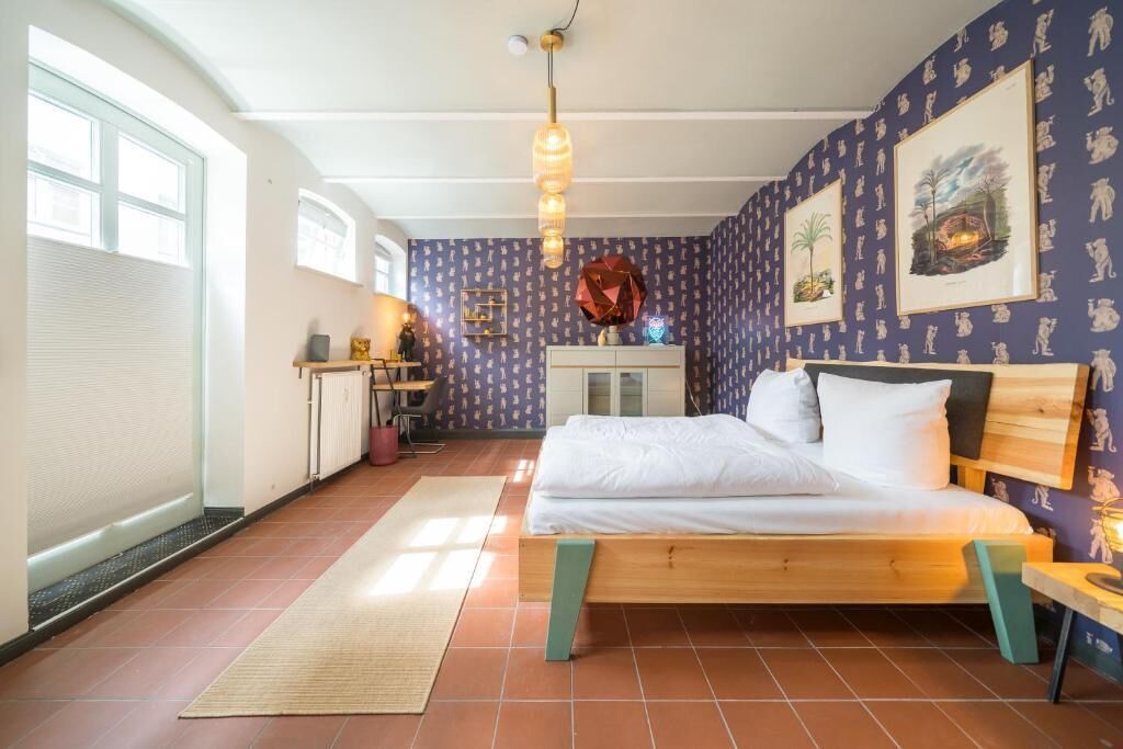 Un dormitorio con una cama de madera, un escritorio, una silla, una ventana y una pared con cuadros.