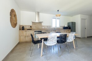 A modern kitchen with a central island, black and white chairs, and a stainless steel range hood. - “Villa des Bourdaines” with Private Pool – Conciergerieland (Vielle Saint-Girons)