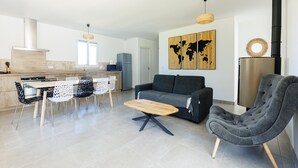 Un salon moderne comprenant un canapé, une table à manger avec des chaises, une table basse en bois, un fauteuil gris, une œuvre d’art représentant une carte du monde, un coin cuisine avec une cuisinière et un réfrigérateur.
