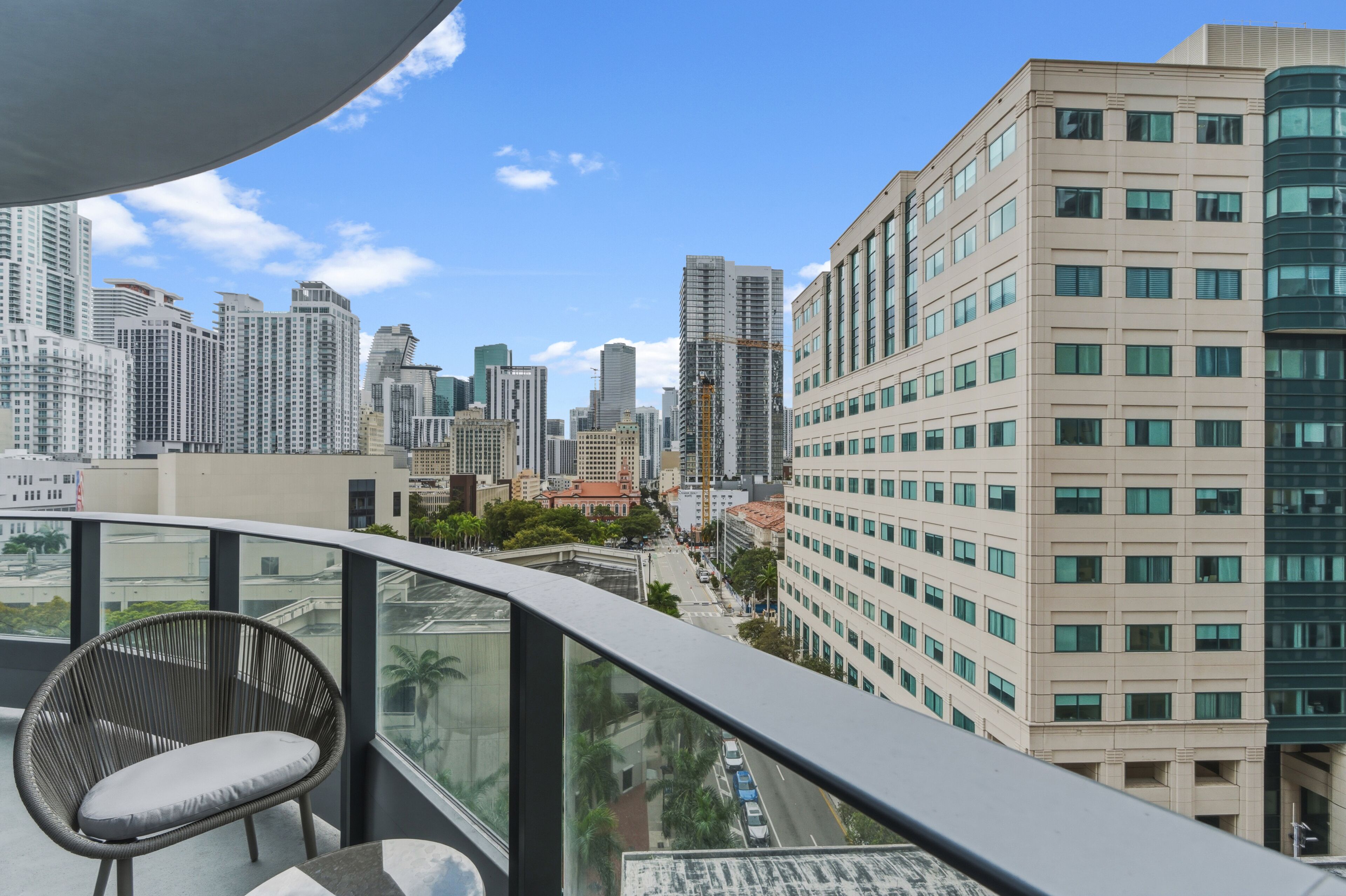 A high-rise building with a balcony, a chair, and a cityscape view.