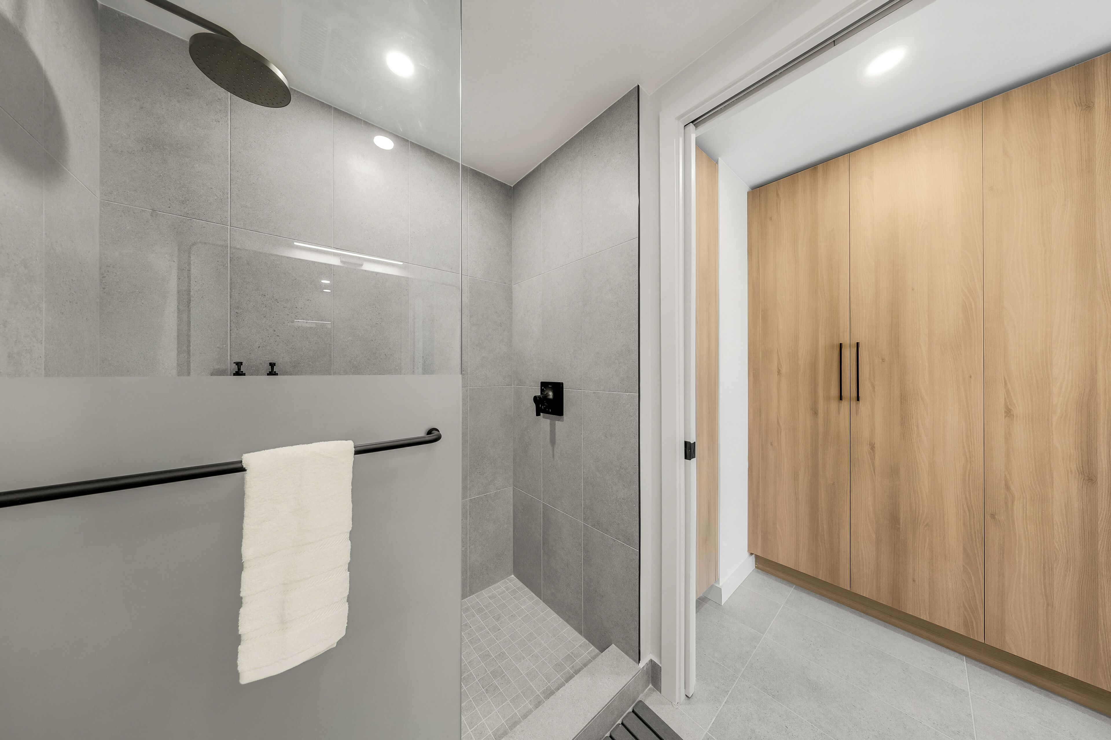 Een moderne badkamer met een glazen douchecabine, een houten garderobe en een witte handdoek aan een metalen handdoekhouder.