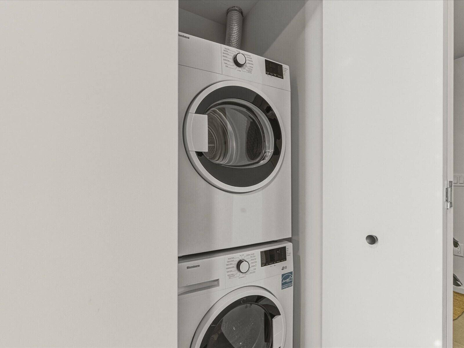 Een gestapelde wasmachine en droger met een bedieningspaneel en een ventilatiepijp.