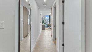 A modern hallway with white walls, a tiled floor, and a view of a cityscape through an open door. - Condo First Downtown Miami (Miami)