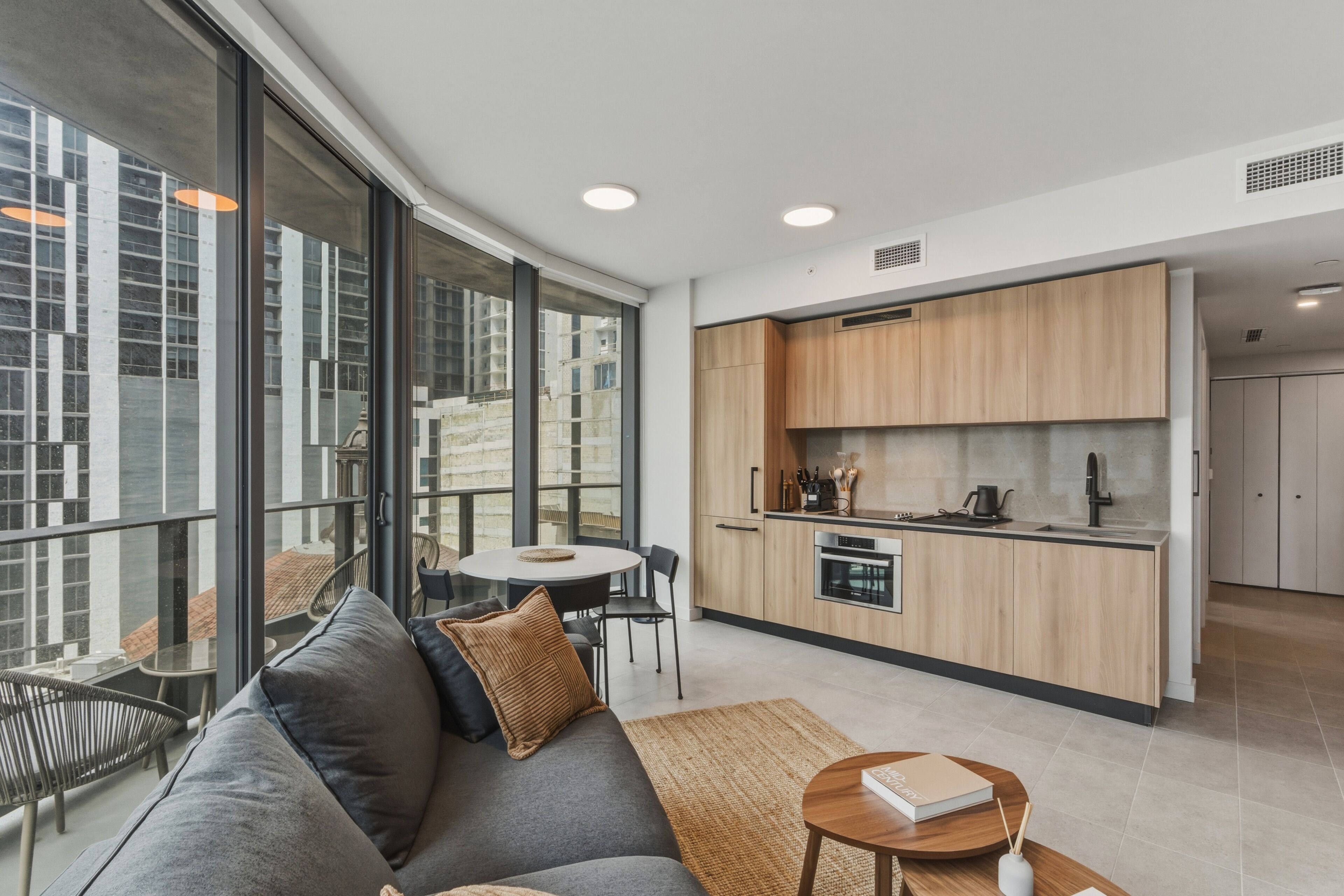 Una cocina moderna con armarios de madera, un comedor con mesa y sillas redondas, y una sala de estar con sofá y mesa de centro.