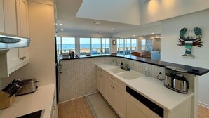 Cocina moderna con vista al océano, que incluye una isla grande, armarios blancos y una cafetera.