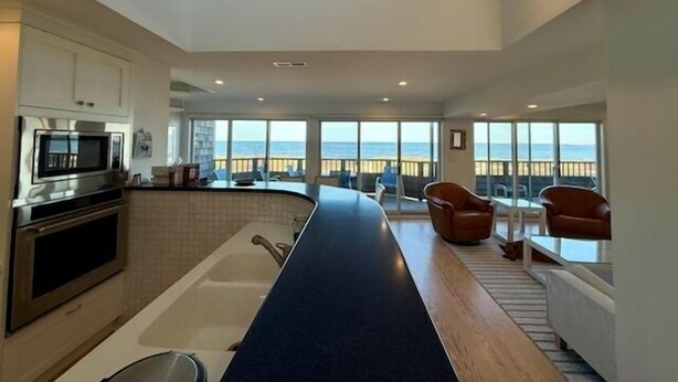 Una cocina moderna con microondas integrado, una isla grande con pileta y vista al océano a través de amplios ventanales.