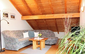 Ein Zimmer mit Holzboden, einer Couch, einem kleinen Holztisch, einer Stehlampe und einem Blumentopf.