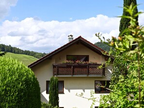 Una casa a due piani con un balcone, immersa nel verde e circondata da colline.