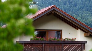 Ett hus med ett sluttande tak, en balkong med träräcken och ett fönster med utsikt över ett skogsbeklätt berg.