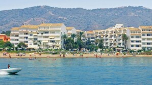 A coastal hotel with multiple balconies, a beach in the foreground, and a mountainous backdrop. - Beach Access Apt in Playa Real | Pool & Terrace - Pass the Keys (Marbella)