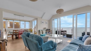 A spacious living room with a large sofa, a coffee table, and a dining area with a table and chairs. - Jarrahdale Beach View Apartment - Pass the Keys (Herne Bay)