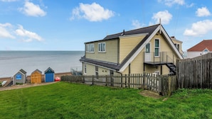 A coastal house with a view of the sea, a wooden fence, and a grassy yard. - Jarrahdale Beach View Apartment - Pass the Keys (Herne Bay)