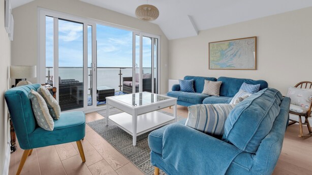 A spacious living room with a large sliding glass door leading to a balcony, a blue sofa set, and a white coffee table. - Jarrahdale Beach View Apartment - Pass the Keys (Herne Bay)