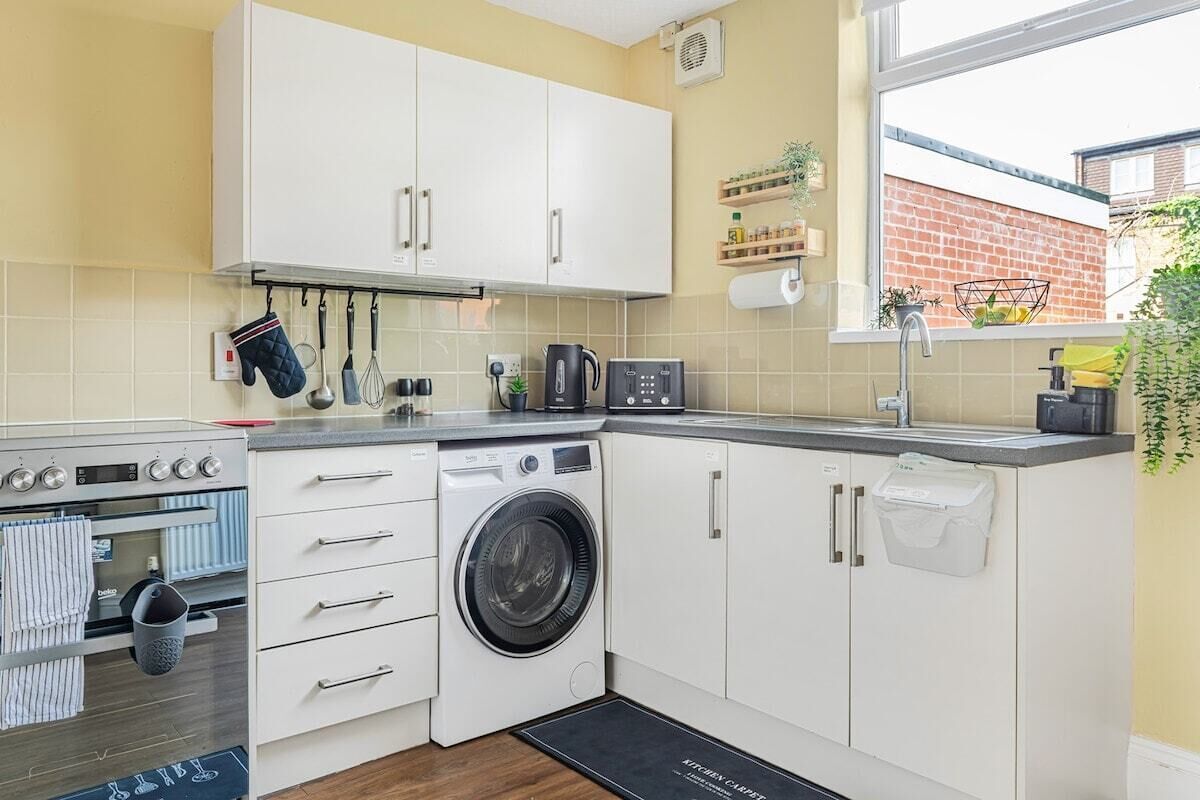 A compact kitchen with white cabinets, a built-in oven, a washing machine, and a coffee maker.