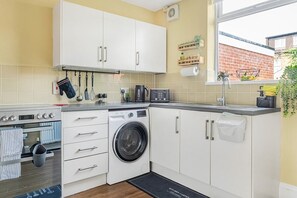 Une cuisine compacte avec des meubles blancs, un four encastré, un lave-linge et une machine à café.