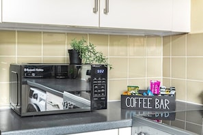 A kitchen with a microwave, a coffee bar, and a potted plant.