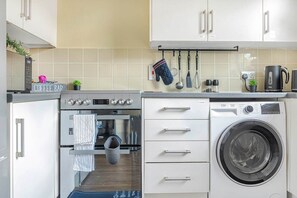 A compact kitchen with a coffee bar, oven, microwave, and washing machine. - Rosewick Villa wt Office, Garden & Free Parking (Nottingham)