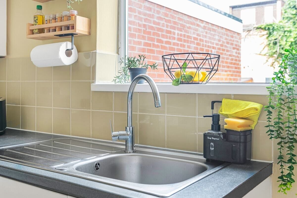 A kitchen with a stainless steel sink, a soap dispenser, a towel holder, and a window with a view of a brick building.