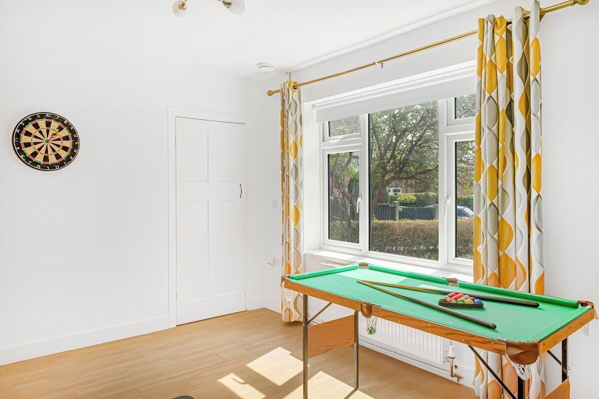 Une pièce avec une table de billard, un jeu de fléchettes et une fenêtre avec des rideaux.