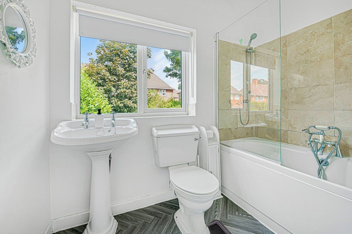 A bathroom with a pedestal sink, toilet, and a glass-enclosed shower area.
