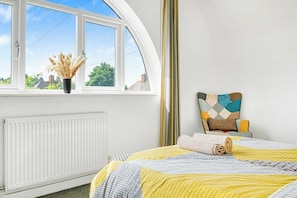 Une chambre à coucher avec un lit, une fenêtre donnant sur un beau paysage, un radiateur et un oreiller fixé au mur.