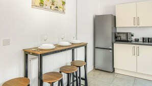 Eine kompakte Küchenzeile mit Essbereich, inklusive Kühlschrank, Schränken, einer Arbeitsplatte und einem Tisch mit Hocker.