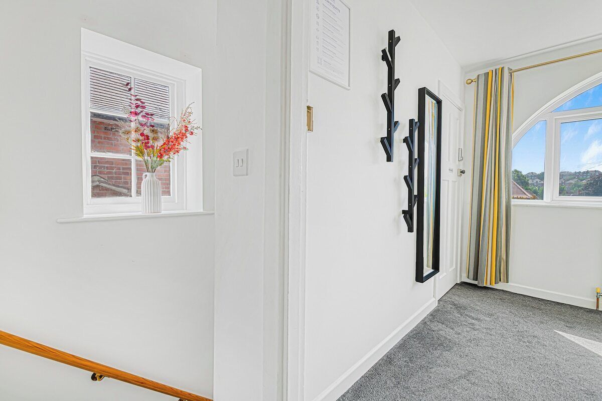 A hallway with a white door, a window with a view of a brick wall, and a black wall-mounted rack.
