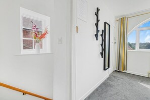 A hallway with a white door, a window with a view of a brick wall, and a black wall-mounted rack.