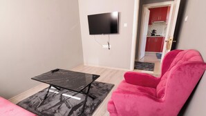 Uma sala de estar com uma mesa de mármore preta, uma poltrona rosa e uma TV fixada na parede.