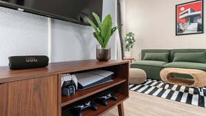Un soggiorno moderno con un mobile TV in legno, un divano verde, un tappeto a scacchi e un quadro incorniciato appeso al muro.