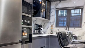 Une cuisine moderne avec un réfrigérateur en acier inoxydable, des armoires noires, un plan de travail en marbre et un tabouret de bar en cuir noir.