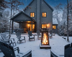 A two-story house with a covered patio area featuring outdoor seating and a central fire feature. - Chalet des Bleuets – Nature Retreat with Spa & Comfort (Petite-Rivière-Saint-François)
